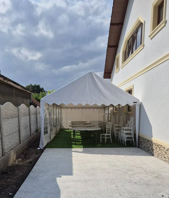 Cort alb montat între casă și gard, cu mese și scaune pregătite pentru amenajare
