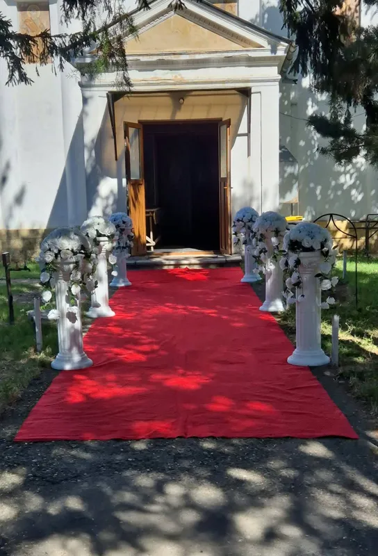 Covor roșu spre intrarea bisericii, mărginit de coloane albe cu aranjamente florale