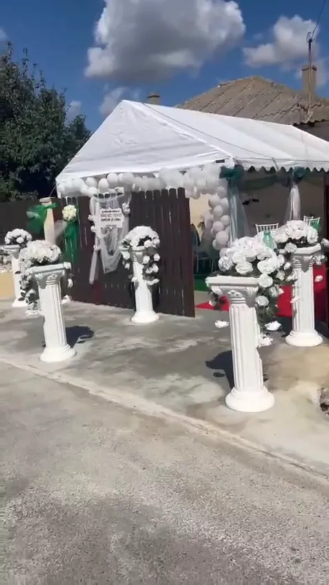 Poster video cu coloane albe și aranjamente florale la intrarea cortului