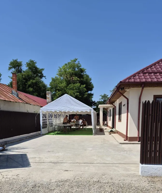 Cort alb în curs de amenajare într-o curte, cu echipa lângă mese
