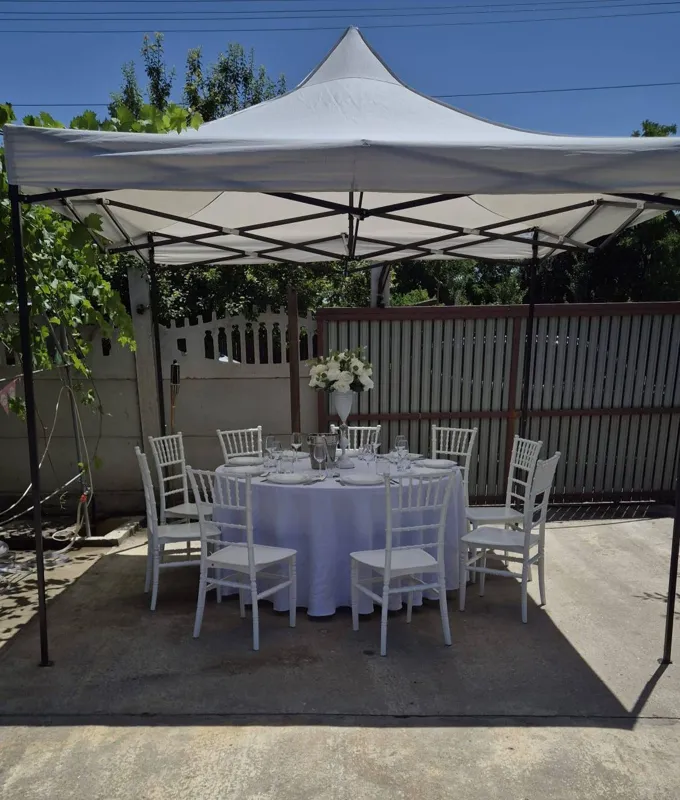 Pavilion alb cu o masă rotundă, veselă, flori albe și scaune albe